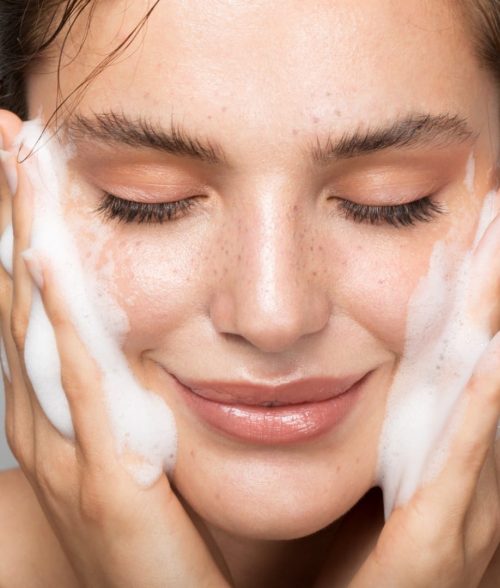 Close up studio shot of a beautiful woman with perfect skin, while she cleaning her face