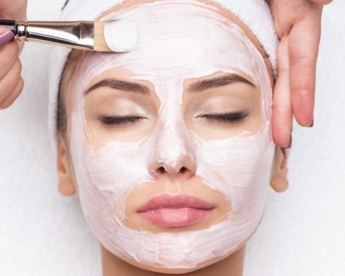 Beautiful young woman receiving facial mask at beauty salon