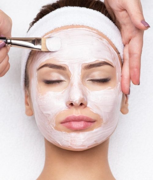 Beautiful young woman receiving facial mask at beauty salon