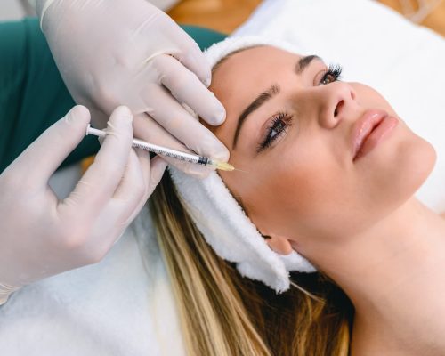 The doctor cosmetologist makes the Rejuvenating facial injections procedure for tightening and smoothing wrinkles on the face skin of a beautiful, young woman in a beauty salon. Hands of cosmetologist are close-ups that inject hyaluronic acid into the cheekbone area of the woman.
