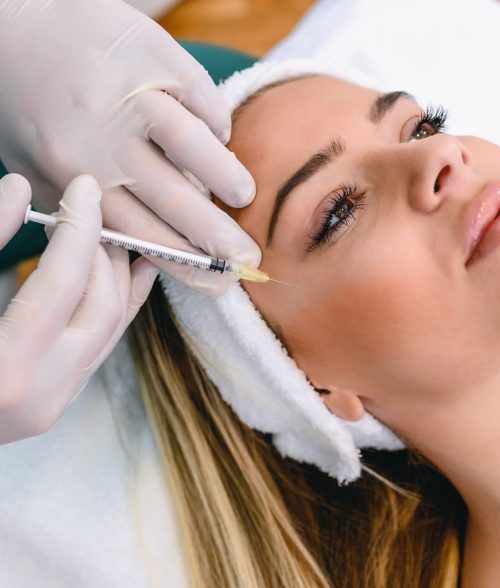 The doctor cosmetologist makes the Rejuvenating facial injections procedure for tightening and smoothing wrinkles on the face skin of a beautiful, young woman in a beauty salon. Hands of cosmetologist are close-ups that inject hyaluronic acid into the cheekbone area of the woman.