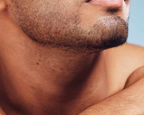 Man, jaw and skincare, face grooming and beard for beauty, aesthetic wellness and healthy skin on studio blue background. Closeup of handsome guy model, facial hair and dermatology body cosmetics